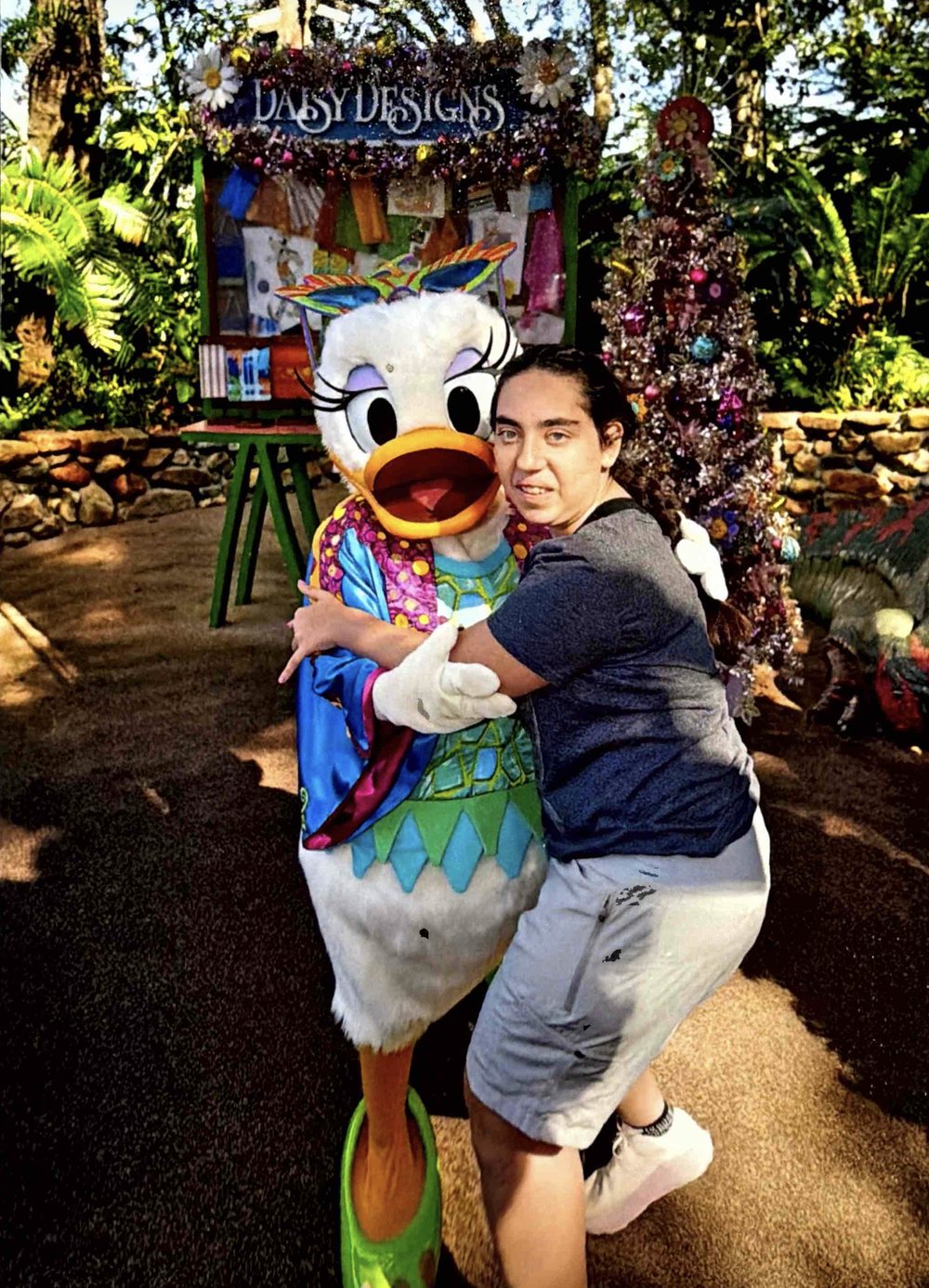 Faith, Dina's daughter, smiling and hugging Daisy Duck in a garden.